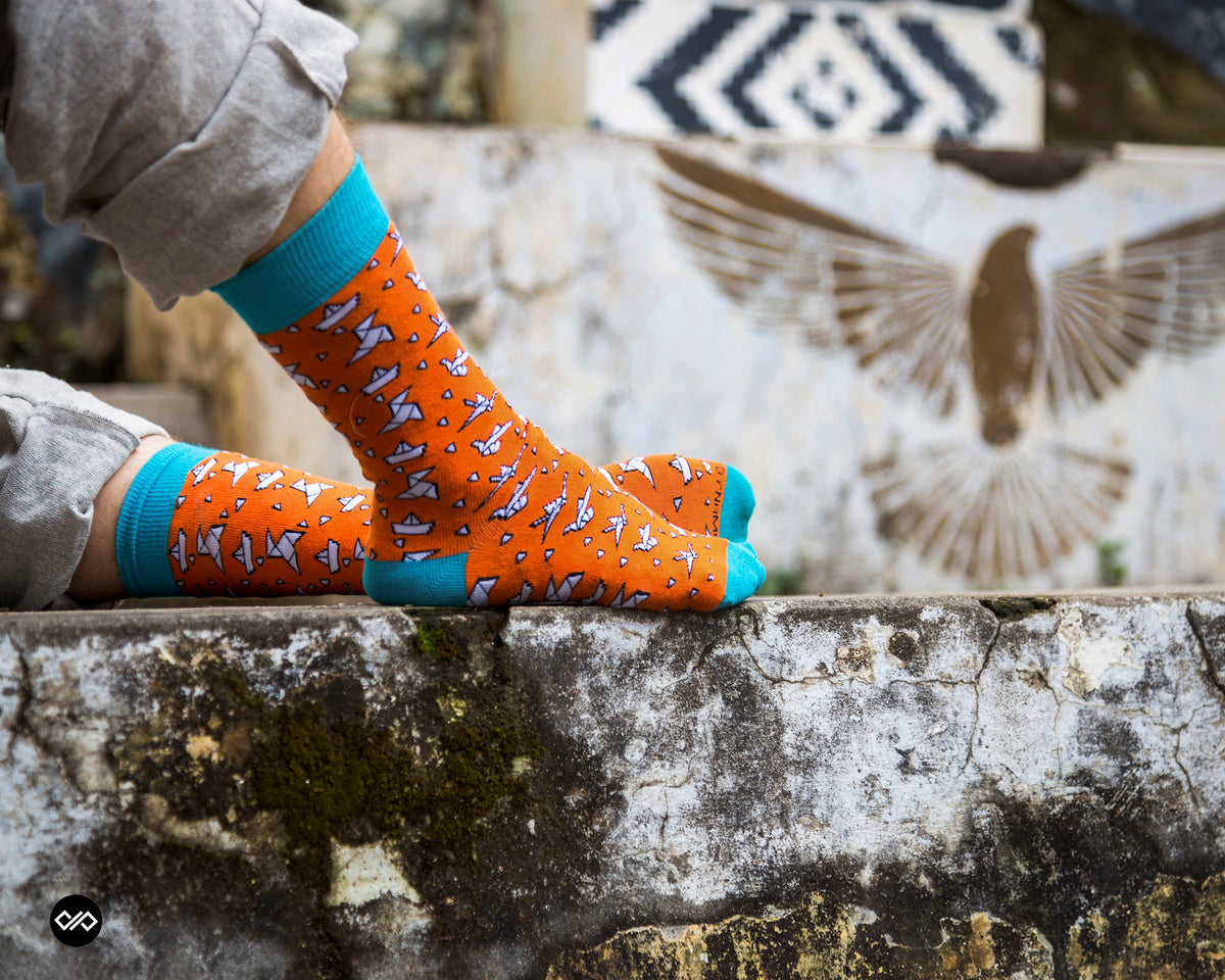 Orange & blue ORIGAMI crew socks worn on feet on a stone ledge