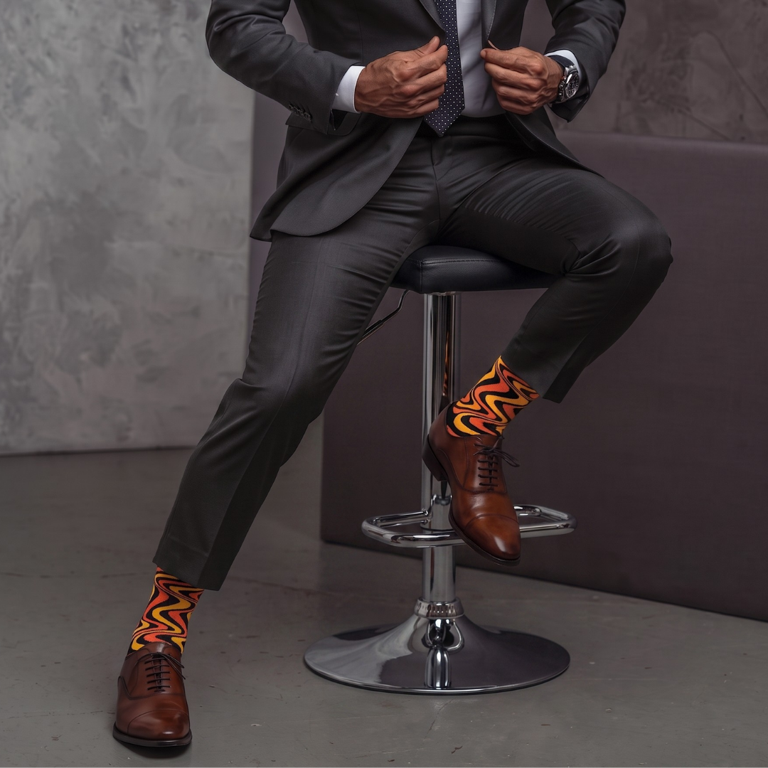 Seated person wearing SIZZLE socks with a grey suit and brown dress shoes