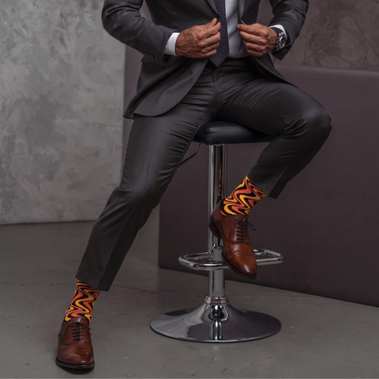 Seated person wearing SIZZLE socks with a grey suit and brown dress shoes
